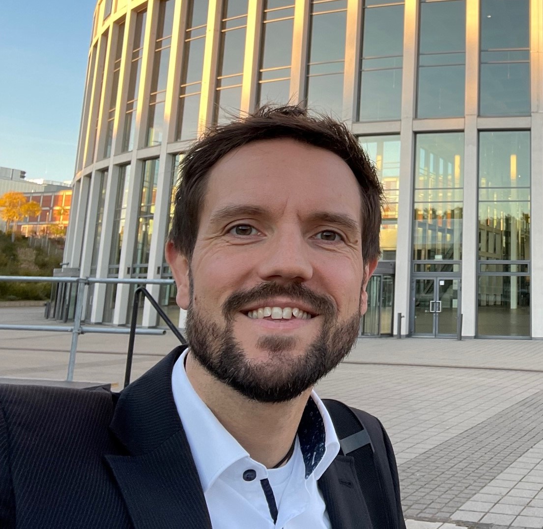 headshot of a man standing in front of a building smiling